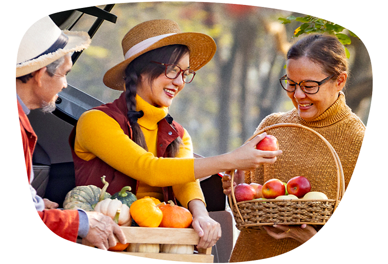Two ladies wearing glasses picking fruits and vegetables at a farmers market.