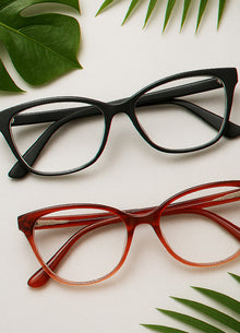 Black and red eyeglasses on a light surface with green leaves.