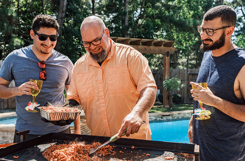 Three men grilling food by a poolside